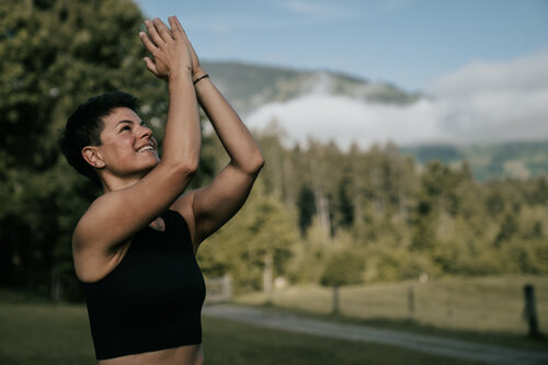 Eine Frau macht Yogaübungen in der Natur. Im Hintergrund sieht man einen Wald und die Bergwelt | © Anna Überegger